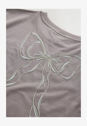 Grå stoftop med et stort, broderet sløjfedesign prydet med sølvperler og lyseblå accenter, glat tekstur.