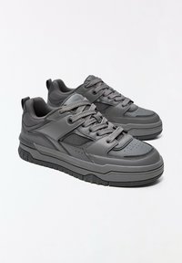 Paire de baskets basses grises avec semelles épaisses, devant à lacets et panneaux latéraux en mesh sur fond blanc.