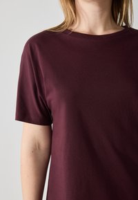 Burgunderfarget t-skjorte med kort erm laget av mykt stoff, med rund hals og standard passform. Glatt tekstur med minimalt med detaljer.