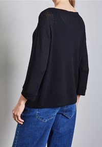 Svart stickad tröja med 3/4-lång ärm, med en lös passform, texturerat tyg och en bred halsringning. Matchad med blå jeans.