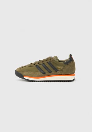 Green suede sneaker with black stripes, orange accents, textured heel, and white sole. Features classic design with lace-up closure.