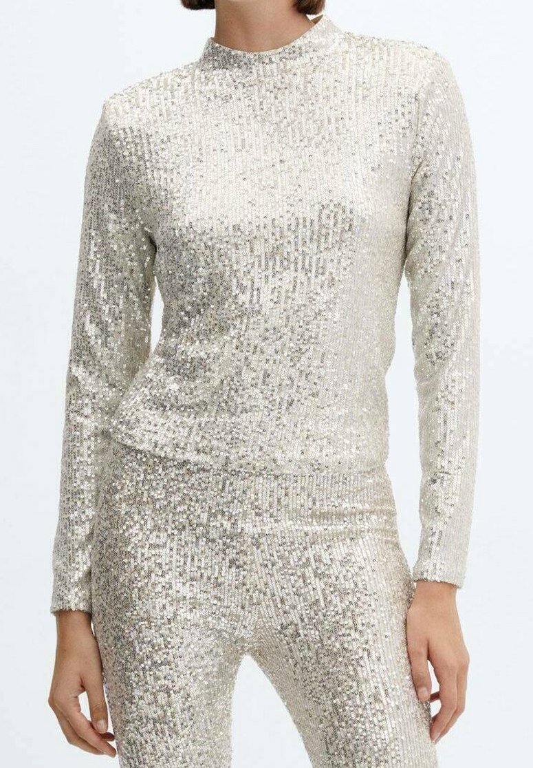 Femme portant un haut à manches longues et col montant et un pantalon assorti couverts de sequins argentés.