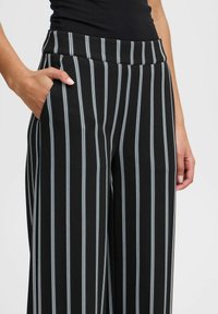 Pantalons larges à rayures noires et blanches avec des rayures d'accent bleu ; dotés d'une taille lisse et d'une poche latérale. Tissu doux et extensible.