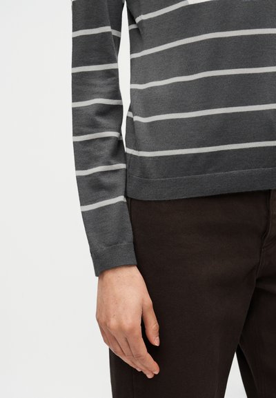 Γκρι ριγέ πουλόβερ με μακριά μανίκια και ανοιχτογκρι οριζόντιες ρίγες. Έχει απαλή υφή και ριμπ μανσέτες, συνδυασμένο με σκούρο καφέ παντελόνι.