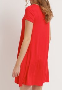 Rotes Kurzarmkleid mit lockerem Schnitt, glatter Textur und fließender Silhouette, das hinten bis zur Mitte des Oberschenkels reicht.