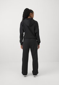 Svart hoodie med en framficka och dragsko, kombinerad med löst sittande svarta sweatpants. Enkel design, mjuk textur och avslappnad passform.