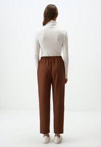 Pantaloni marroni con vita elastica e design affusolato. Indossati con un dolcevita bianco a coste e sneakers bianche. Texture liscia, stile casual.