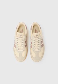 Kremaste superge z rožnatimi poudarki, z zgornjim delom iz teksturirane usnjene površine, trirazdelnim dizajnom in gumijastim podplatom. Škornji so ravni in ploskvi.