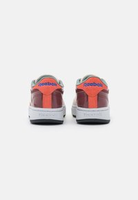 Röda lackläder sneakers med gröna detaljer och orange häl. Har en vit sula med "Reebok" präglat på baksidan.