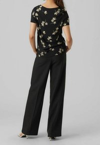 Top negro de manga corta con estampado floral, combinado con pantalones negros de pierna ancha. El top tiene un escote redondeado y un corte relajado.