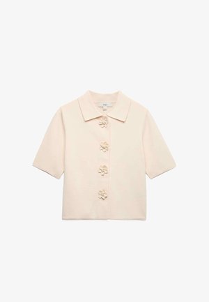 Blusa de manga corta color crema con cuello puntiagudo y cuatro botones decorativos en forma de flor en la parte delantera.
