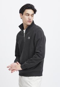 Zwarte kwart-rits sweatshirt met een gestructureerd oppervlak, voorzien van een logo op de borst, ribgebreide manchetten en zijnaden voor een aansluitende pasvorm.