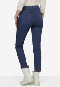 Námořnické modré tapered džíny s bočními pruhy, zadními kapsami a vysokým pasem. Noseny s bílými gumovými kotníkovými botami. Hladká, elastická látka.