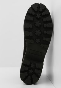 Černá gumová podešev s hlubokým, drsným vzorem a vyvýšenými tvary hvězd; hladký, tmavý svrchní materiál se jemnou texturou.