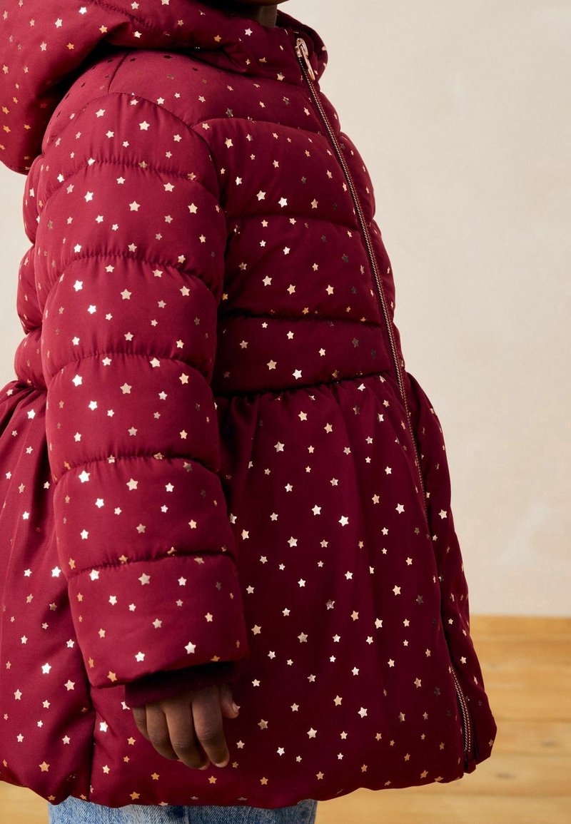Blouson matelassé bordeaux avec une taille ajustée, arborant des motifs d'étoiles dorées, une fermeture éclair et une capuche. Texture douce avec un design matelassé.