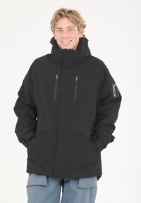 Musta vedenpitävä takki korkealla kauluksella, kahdella vetoketjullisella etutaskulla ja säädettävillä hihansuilla. Suunniteltu ulkoilma-aktiviteetteihin, teksturoitu kangas.