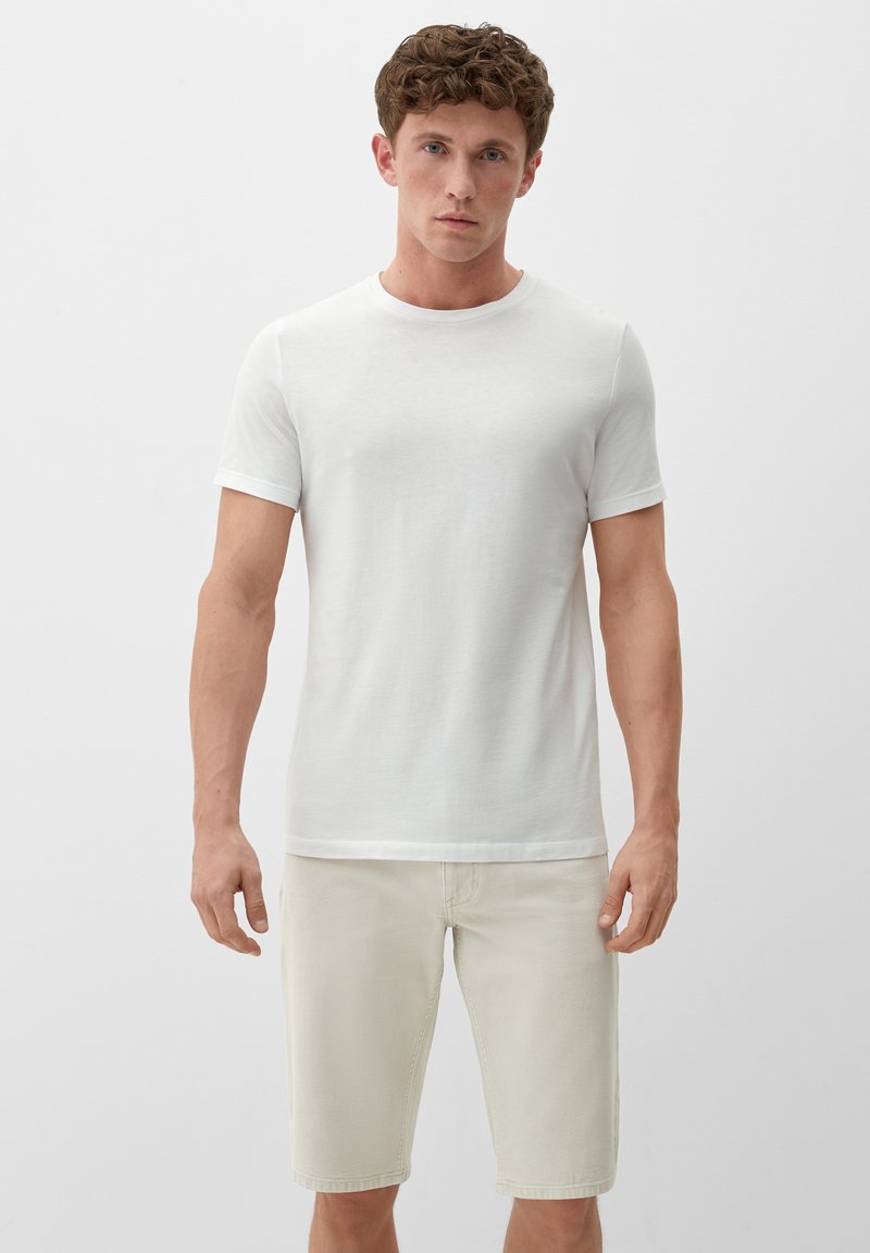 Weißes T-Shirt mit kurzen Ärmeln aus weicher Baumwolle, kombiniert mit hellbeigen, knielangen Shorts, die ein einfaches und figurschmeichelndes Design aufweisen.