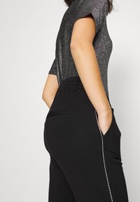 Czarne spodnie z błyszczącą, krótką bluzką z krótkim rękawem. Spodnie mają boczne kieszenie i ozdobną linię z cyrkonii wzdłuż szwu.