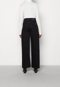 Svart jeans med vida ben och hög midja, tillverkade av denim. Har bakfickor och en etikett på midjebandet. Bärs ihop med en vit långärmad topp.