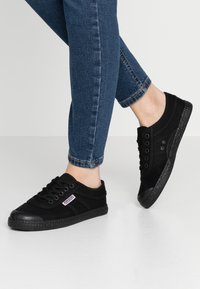 Sneakers neri in tela con punte in gomma e suole testurizzate. Le caratteristiche includono un classico design con lacci e un dettaglio a striscia laterale.