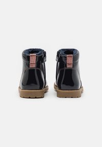 Černé lakované kotníkové boty s měkkým modrým interiérem, třpytivým růžovým poutkem na patě a gumovou podrážkou s protiskluzovým vzorem.