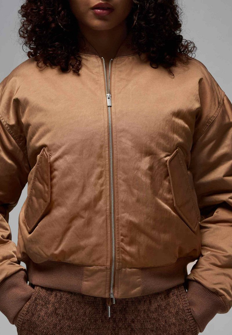 Veste bombardier marron avec fermeture éclair à l'avant, deux poches latérales, poignets côtelés et texture douce et lisse.