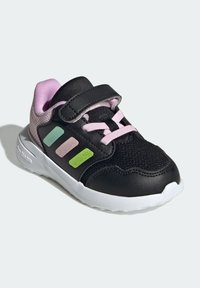 Chaussure de sport noire en mesh et matériaux synthétiques. Présente des accents roses, trois bandes colorées (vert, sarcelle, rose) et une semelle blanche.