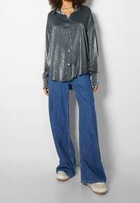 Metallic silver skjorta med knappar och lös passform, kombinerad med vida blå jeans och vita platåskor. Slät textur och avslappnad stil.