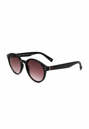 Occhiali da sole rotondi neri con lenti a gradiente scuro e un piccolo dettaglio a forma di cuore rosso sulla stanghetta, su sfondo bianco.