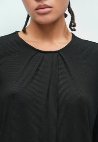 Top negro acanalado con un escote redondo y pliegues a lo largo del corsé. La tela tiene una textura suave y un brillo sutil.