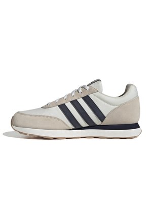 Zapatillas de ante beige y cuero blanco con franjas azules, cuello acolchado y cordones blancos, presentan una suela de goma texturizada.
