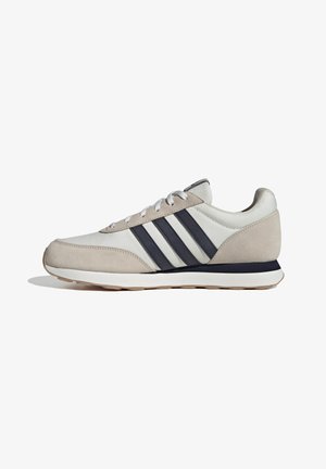 Zapatillas de ante beige y cuero blanco con franjas azules, cuello acolchado y cordones blancos, presentan una suela de goma texturizada.