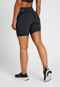 Svarta ribbade träningsshorts med hög midja, med vita accentlinjer och ett geometriskt mönster på sidorna. Bärs med svarta skor.