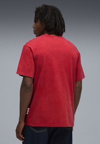 Rød bomulds T-shirt med en afslappet pasform, korte ærmer og en subtil falmet tekstur. Har et sidelabel nær kanten.