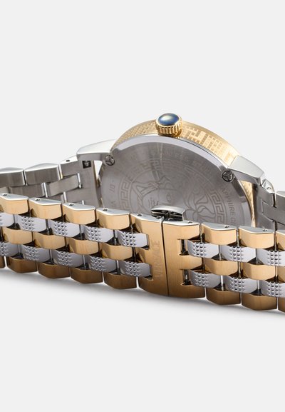Orologio in metallo dorato e argentato con retro decorato, cassa rotonda, corona blu e bracciale a maglie decorative. Presenta dettagli incisi sul retro.