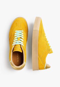 Sneakers in suede giallo con lacci azzurri chiari e suola in gomma testurizzata. Presentano dettagli in tan sulla parte posteriore e sulla linguetta, insieme a cuciture decorative.