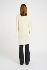 Maglione lungo color crema con un lavorazione a maglia testurizzata, caratterizzato da una linea dritta e maniche larghe, abbinato a jeans neri a palazzo.
