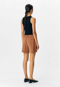 Shorts marron avec une taille élastique et des poches arrière, associés à un haut sans manches noir. Tissu lisse, coupe décontractée, longueur jusqu'aux genoux.