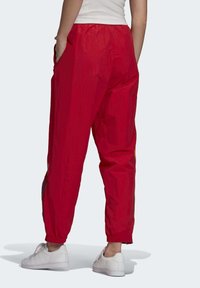 Červené sportovní kalhoty s elastickým pasem, s bočními kapsami a manžetami na zápěstích, vyrobené z hladkého, lehkého materiálu. Nosit bílé tenisky.