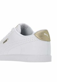 Białe sneakersy z gładką skórzaną cholewką, złotym akcentem na pięcie i perforowanymi detalami. Posiadają gumową podeszwę i sznurowanie.
