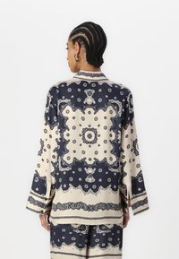 Navy and cream patterned shirt made of smooth fabric, featuring long sleeves, a collar, and intricate designs with circular motifs.