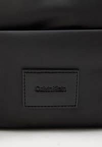 Fekete nylon táska, texturált Calvin Klein logóval, téglalap alakú, sima, matt felülettel.