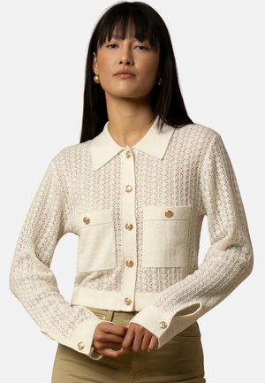 Cardigan avorio con motivo in pizzo, bottoni tono oro, colletto e tasche frontali. Maniche lunghe con polsini abbottonati. Tessuto a maglia texturizzato.