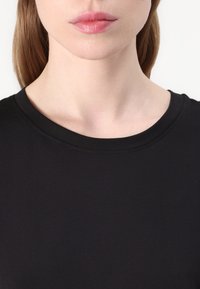 Svart t-skjorte med rund hals, laget av glatt stoff. Har korte ermer og en slank passform rundt halsen og skuldrene.