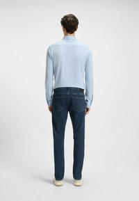 Lys blå langermet skjorte kombinert med mørkeblå jeans. Skjorten har krage, mens jeansene har en klassisk passform og baklommer.