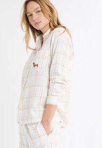 Biała flanelowa koszula nocna w beżową kratkę, z zapięciem na guziki i kieszenią na piersi z haftowanym brązowym wzorem psa.