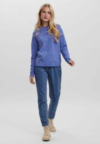 Blue knit sweater with a crew neckline, combined with light blue denim jeans and beige sneakers. Textured surface and casual fit.