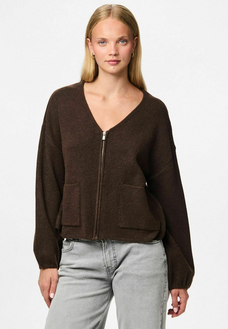 Brūns adīts kardigāns ar V veida kaklu, ar rāvējslēdzēju un divām priekšējām kabatām. Īpašības: vaļīgas piedurknes un īss dizains. Mīksta faktūra.