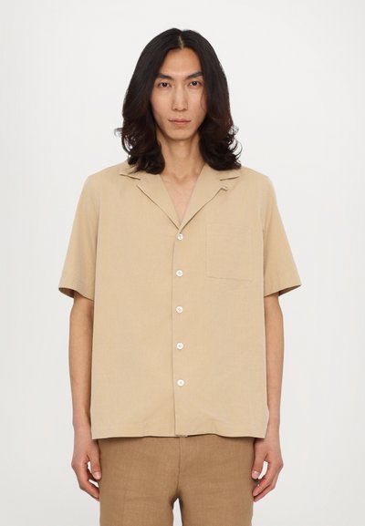 Korte mouwen beige shirt van gestructureerde stof, met een zak, notch kraag en witte knopen tegen een effen achtergrond.