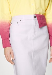 Henkilö, jolla on valkoinen korkeavyötäröinen hame ja pitkähihaiset paita, jonka väri liukuu keltaisesta pinkkiin, ja paita on osittain sujautettu ulos toiselta puolelta.